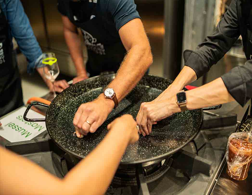 Photo of a cooking team building in Barcelona: participants cook a paella in a group as a corporate activity. Ideal for company events with dietary options (vegan, vegetarian, seafood, meat and gluten-free) and flexible schedules.