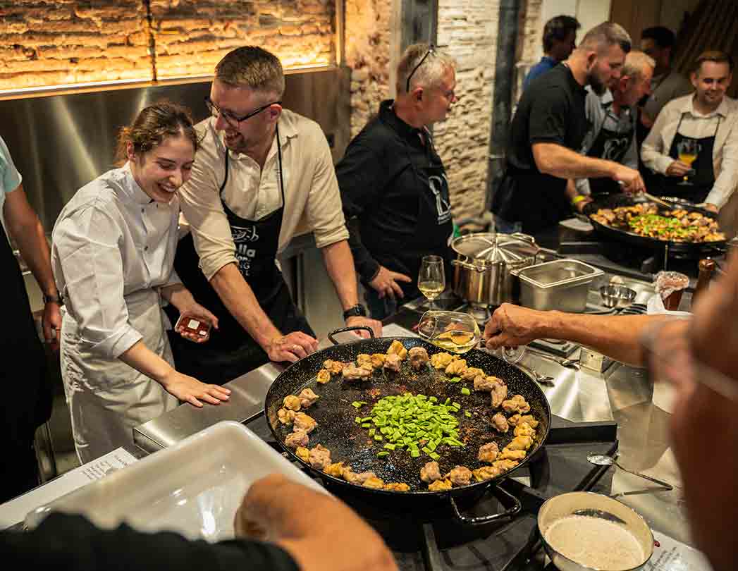 Foto de un taller de paella para empresas en Barcelona con el equipo reunido alrededor de una paellera circular. La dinámica tipo “mesa redonda” favorece la interacción cara a cara, difumina jerarquías y centra el enfoque colectivo en un objetivo común: cocinar juntos una paella.
